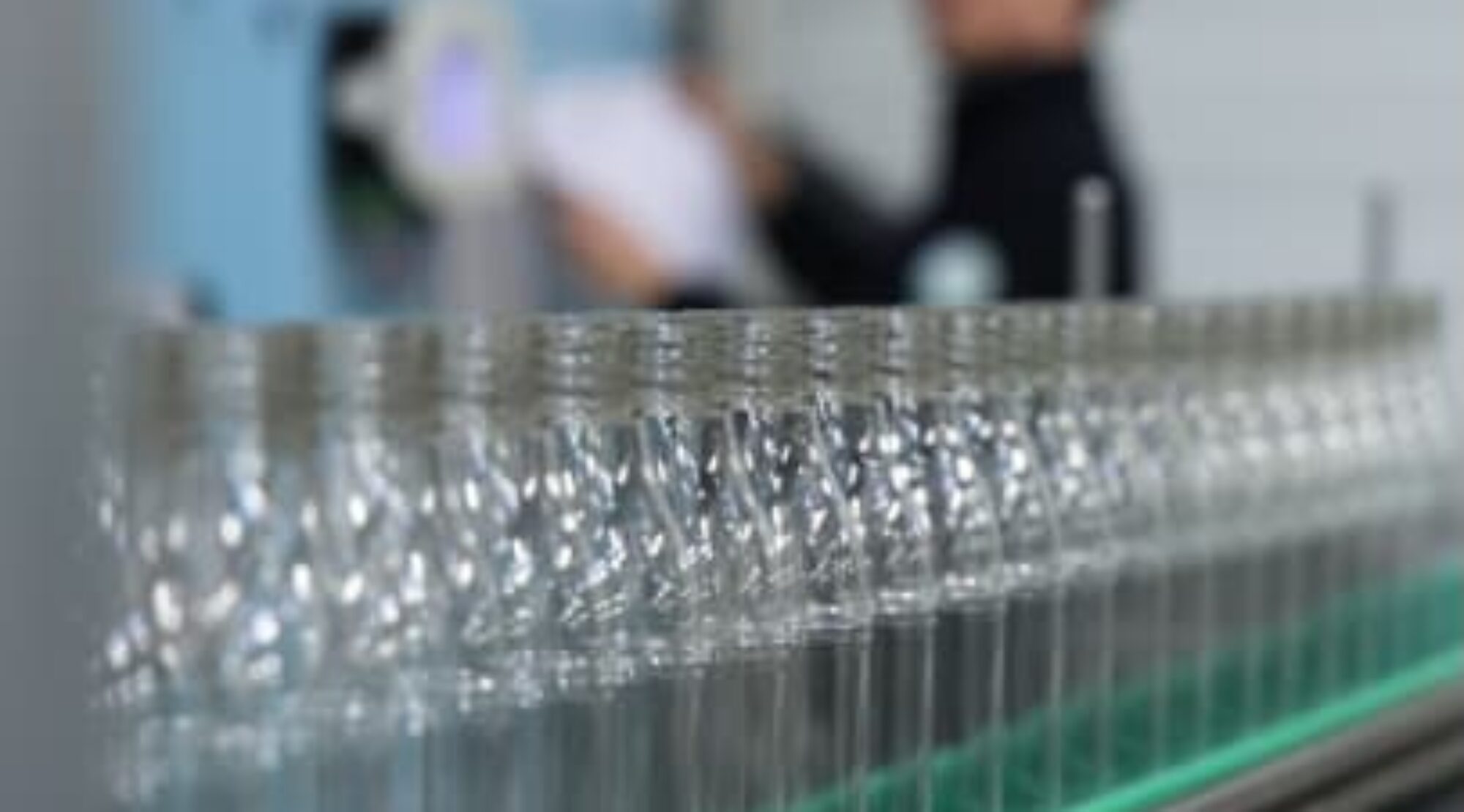 Vue rapprochée d'une chaîne de production industrielle alignant des bouteilles plastique PET transparentes, prêtes pour le remplissage ou l’étiquetage